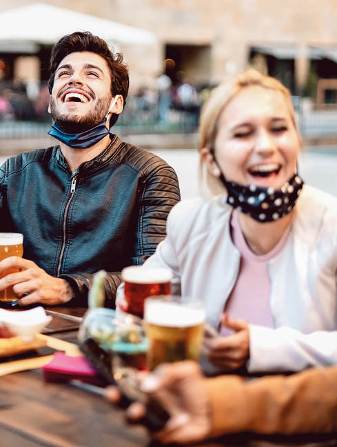 Young friends drinking beer wearing face mask - New normal lifestyle concept with people having fun together talking on happy hour at outside brewery bar - Bright warm filter with focus on central guy
